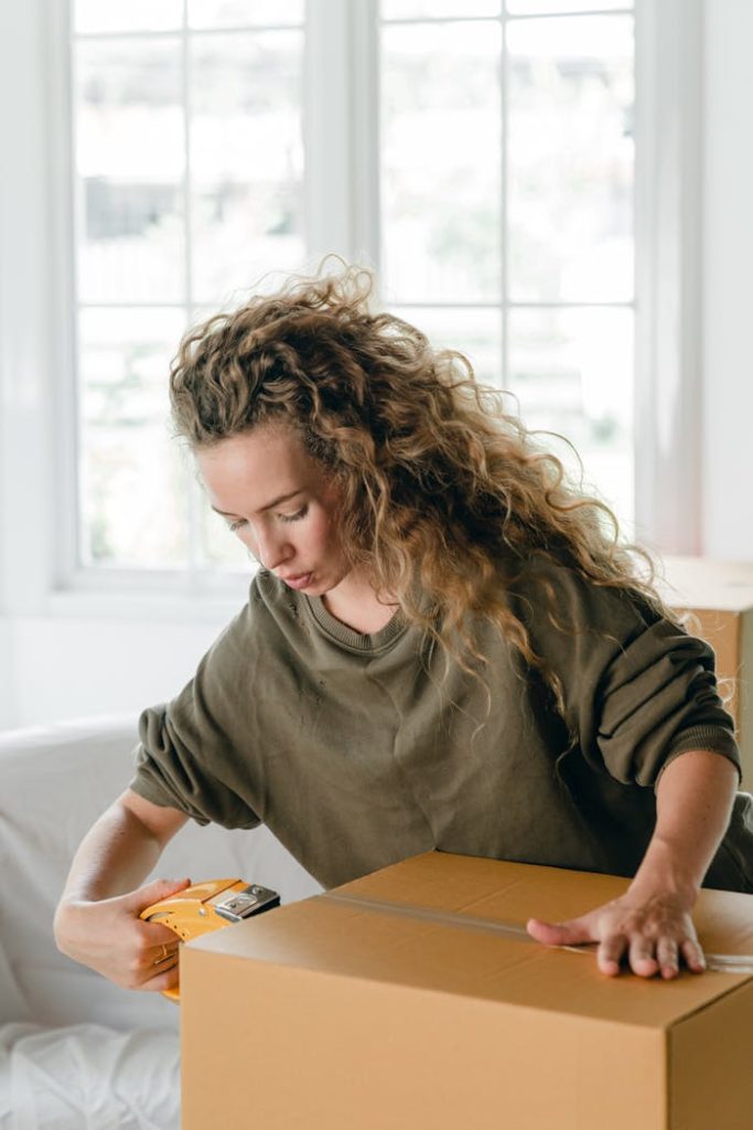 Young woman concentrating while packing a cardboard box at home for relocation.